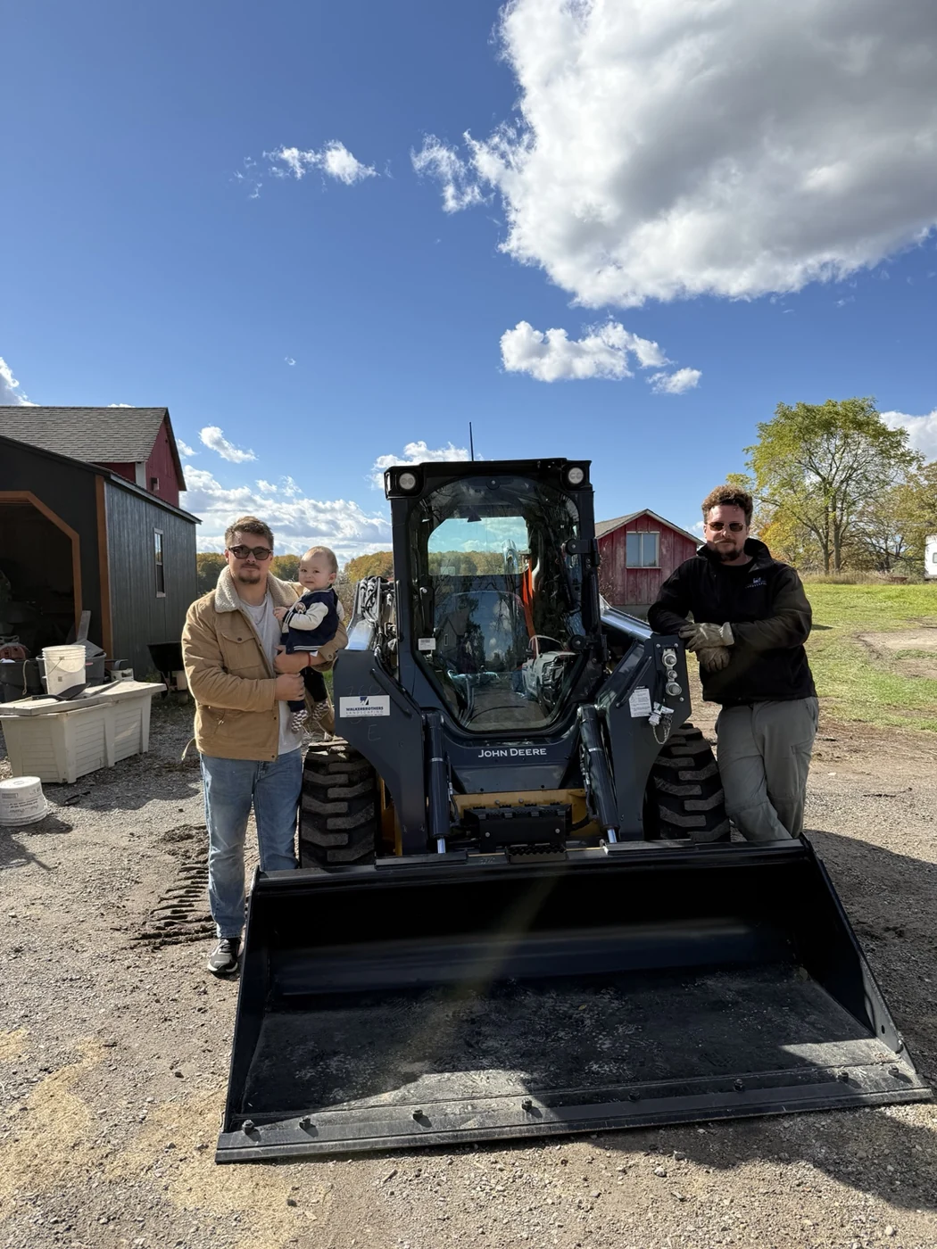The Walker brothers standing beside their John Deere skid steer, with a child held by one brother