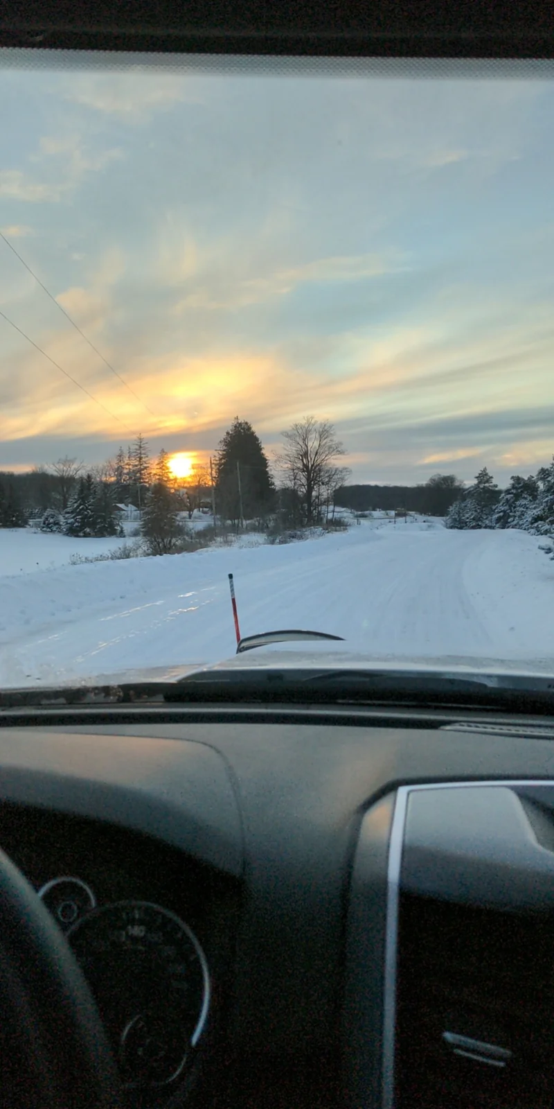 Real photograph from inside a truck looking along a snowy road beneath a golden winter sunset